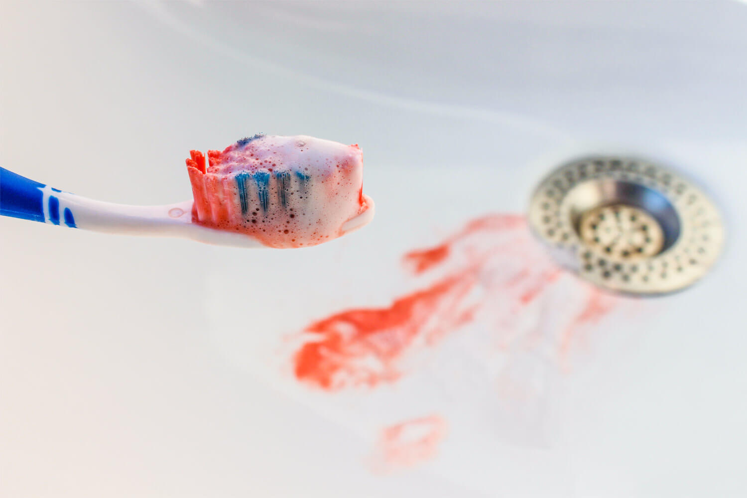 Toothbrush with blood on the bristles and blood in the sink from gum disease