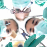 Looking up into a group of dentists performing oral surgery in green scrubs with special tools