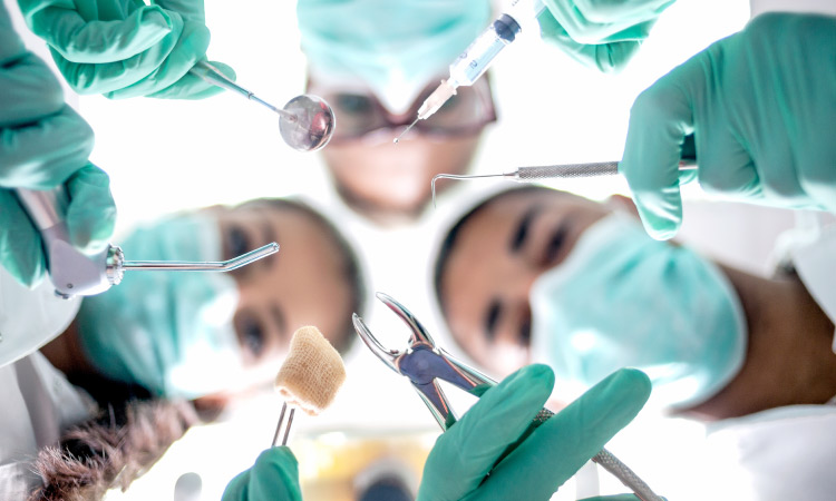 Looking up into a group of dentists performing oral surgery in green scrubs with special tools in jonesboro