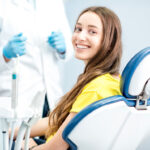 Brunette white woman in a yellow shirt smiles while sitting in a dental chair at the dentist