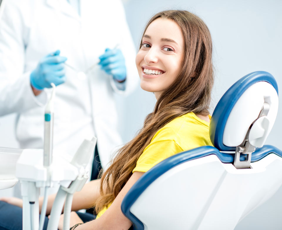 Brunette white woman in a yellow shirt smiles while sitting in a dental chair at the dentist in jonesboro