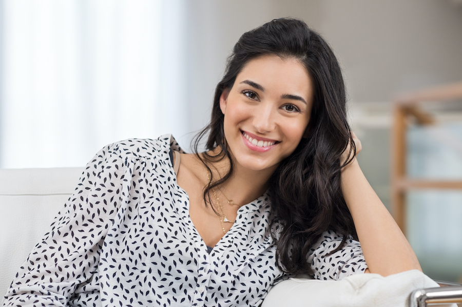 Smiling dark-haired woman in a black and white blouse leans on her elbow on a couch in jonesboro