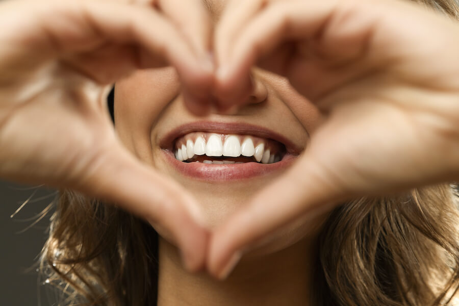 A woman holds her hands in a heart shape in front of her smile
