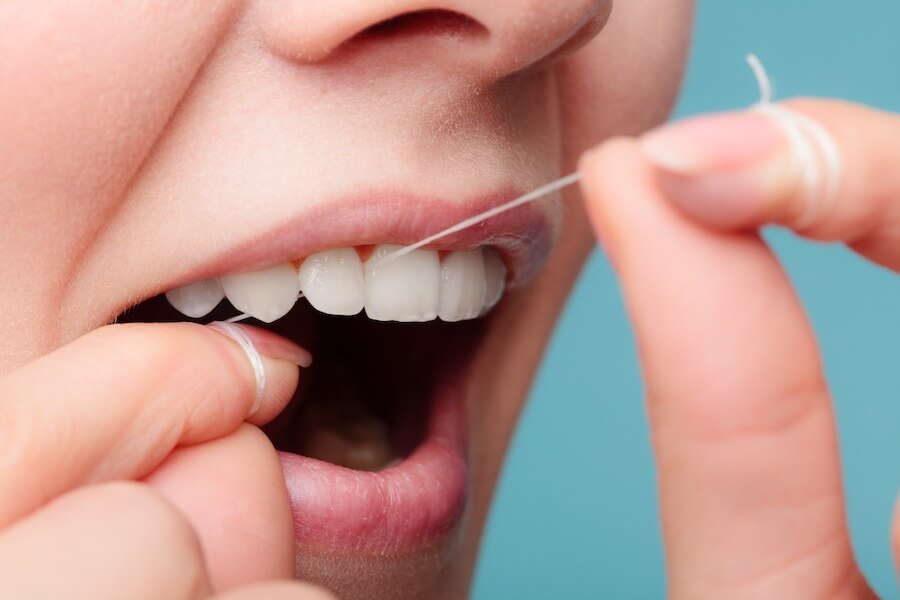 Closeup of woman using string floss to clean between her teeth against a blue background