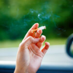 Closeup of a woman's hand holding a smoking cigarette near a car window