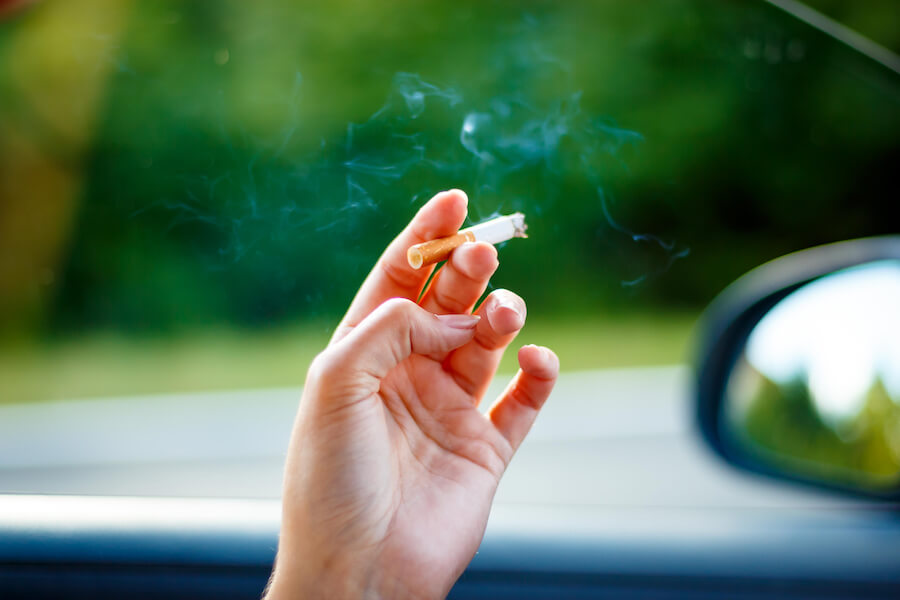 Closeup of a woman's hand holding a smoking cigarette near a car window in jonesboro