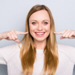 Blonde woman smiles and points horizontally to her teeth in jonesboro