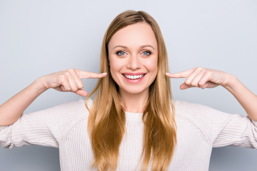 Blonde woman smiles and points horizontally to her teeth