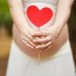 Photograph of pregnant woman's belly with a stick with a red heart on top.